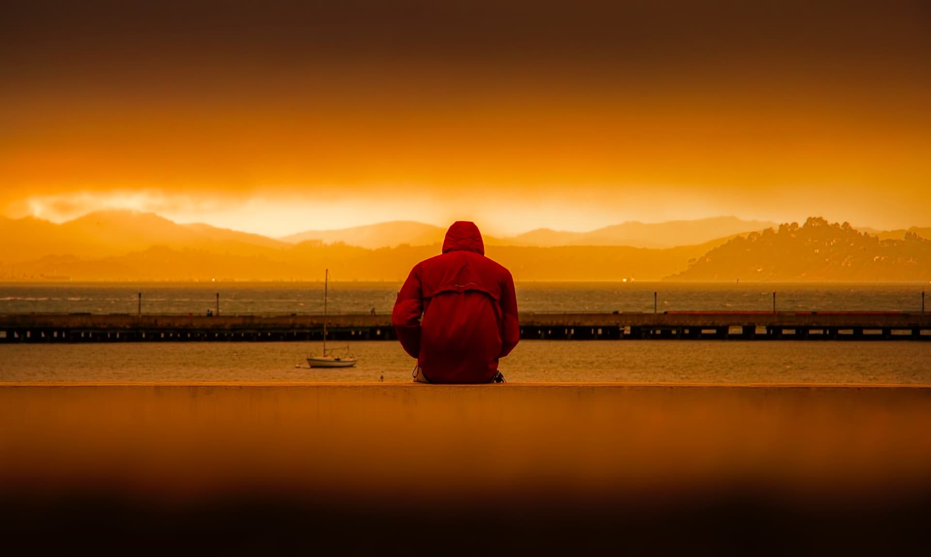 person wearing red hoodie sitting in front of body of water